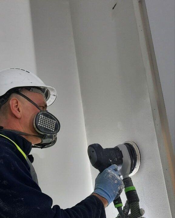 Vitalii in a hard hat and dust mask, skimming a wall on site